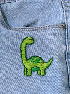 a green dinosaur embroidered on the back pocket of a pair of blue denim jeans,