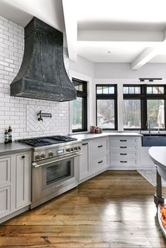 a large kitchen with white cabinets and stainless steel stove top hood over an island in the middle