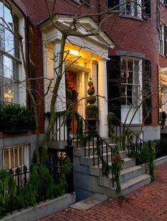 a red brick house with white trim and black shutters on the front door is lit up at night