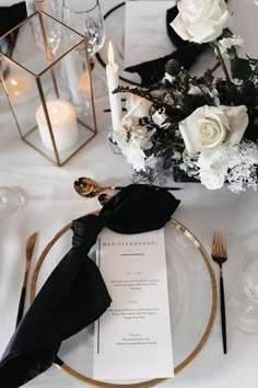 a table setting with black and white flowers, gold rimmed place settings and candles