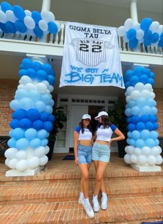 two young women standing in front of a building with blue and white balloons on it