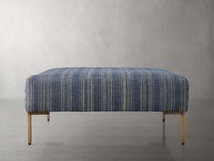 an upholstered footstool with wooden legs and a blue striped fabric cover