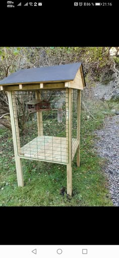 a small wooden bird cage with a roof on the grass and trees in the background