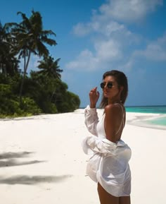 a woman standing on top of a sandy beach next to the ocean and palm trees