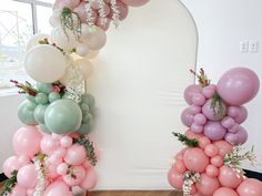 balloons and greenery are arranged in front of a white backdrop for a balloon arch