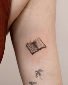 a woman's arm with an open book and butterflies tattoo on her left side