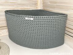 a large gray basket sitting on top of a white table next to a wooden wall