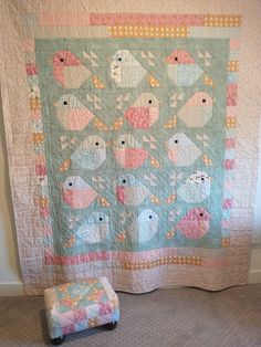 a quilted wall hanging next to a footstool in a room with carpet