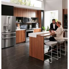 a man and woman sitting at a kitchen counter looking at something on the tabletop