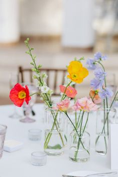 colorful flowers in vases on a white table cloth with place cards and silverware