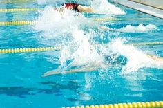 people are swimming in the pool with their backs turned to the side, and one person is jumping into the water