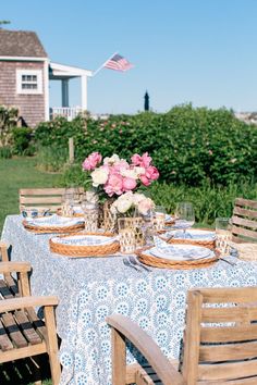 a table set with flowers and plates on it in front of a house near the ocean