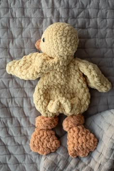 a crocheted stuffed duck on a quilted bedding with gray and white sheets