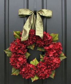 a wreath with red flowers and green leaves is hanging on the front door's black door