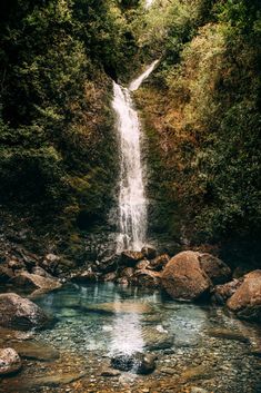 a waterfall in the middle of a forest with rocks and water running down it's sides