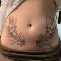 a woman's stomach with flowers and leaves tattooed on the side by her belly