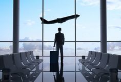 a man with a suitcase standing in an airport terminal looking out the window at the sky