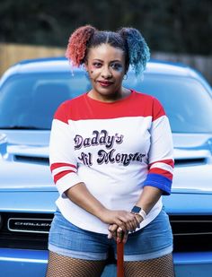 a woman standing in front of a blue car with her hands on the handlebars