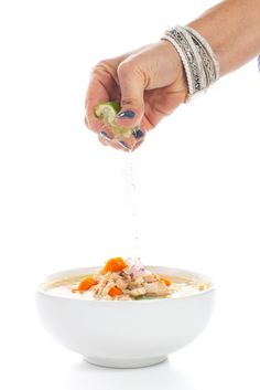 a person is sprinkling something into a bowl of soup with carrots and celery