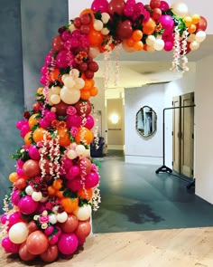 an arch made out of balloons and flowers in the middle of a room with a mirror