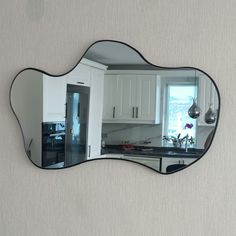 a mirror reflecting a kitchen with white cabinets and black counter tops on the wall in front of a window