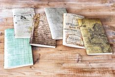 four notebooks sitting on top of a wooden table covered in old maps and writing