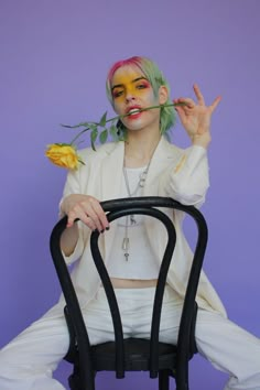 a woman sitting on top of a chair with her hands in the air while holding a flower