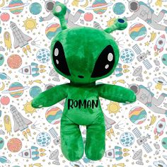 a green stuffed animal with the word roman on it's chest and eyes, surrounded by space objects