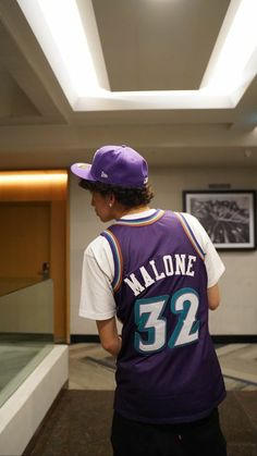 a young man in a purple jersey and hat looking at something on the wall behind him