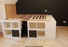 an unfinished bed frame with drawers and shelves on the bottom side in a room that is painted black