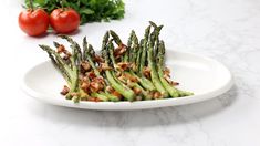 someone is cutting asparagus on a plate with tongs and tomatoes in the background