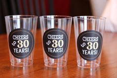 three shot glasses with cheers and 30 years stickers on the bottom, sitting on a table