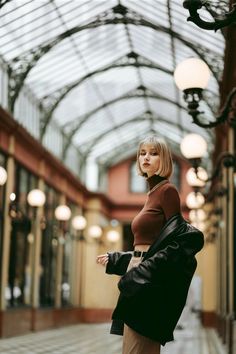 a woman is standing in the middle of an indoor area wearing a brown top and tan pants