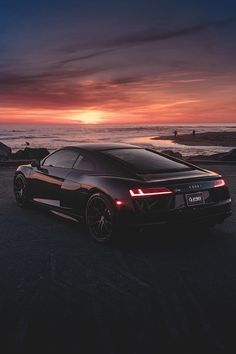 a black sports car parked in front of the ocean at sunset with people swimming in the water