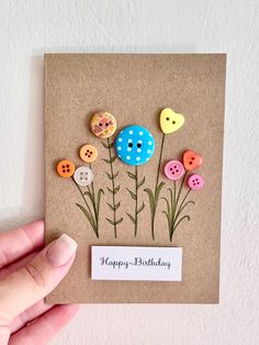 a hand holding a card with buttons and flowers on it that says happy birthday,