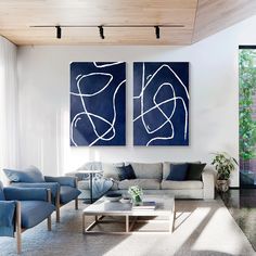 two paintings hang on the wall above a couch in a living room with blue and white furniture