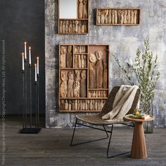 a chair and table in front of a wall with wooden carvings on it, surrounded by candles