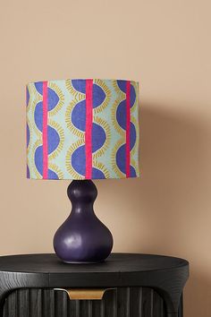 a purple table lamp sitting on top of a night stand next to a black cabinet