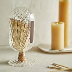 a glass vase filled with matches on top of a table next to two candles and some sticks