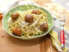 a green bowl filled with spaghetti and meatballs on top of a wooden cutting board