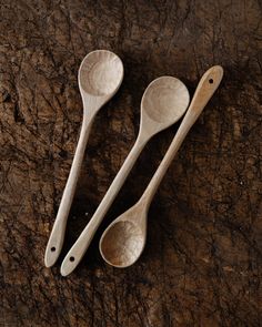 three wooden spoons sitting on top of a piece of wood next to each other