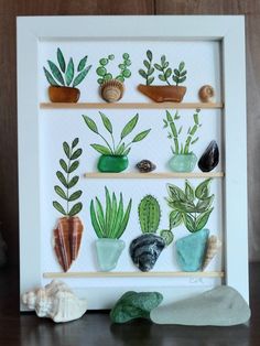 a white frame with some plants and rocks in it on a shelf next to a wall