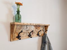 a coat rack with hooks and flowers in a vase on the wall next to a denim jacket