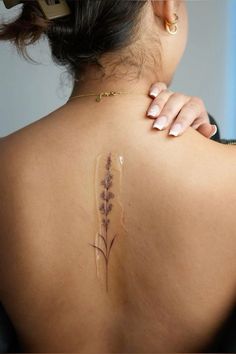 the back of a woman's shoulder with a tattoo on her left arm and purple flowers