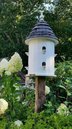 a white bird house sitting on top of a wooden pole in the middle of flowers