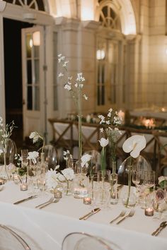 the table is set with clear vases and white flowers in glass containers on each side