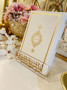 an open book sitting on top of a table next to flowers and a gold plate