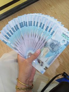 a person holding several bills in their hand on a wooden floor next to a purse