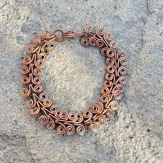 a close up of a metal bracelet on a stone surface with some wire wrapped around it