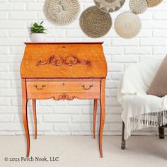 there is a small wooden desk in front of a white brick wall with lots of decorative items on it